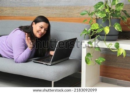 Single Latin adult woman uses her laptop on the couch at home to do home office, shop online, make video calls, make romantic dates
