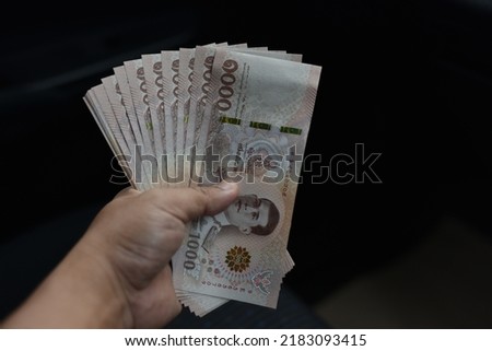 Hand holds money thai baht 1000 banknotes. One thousand THB. Business concept. currency in Thailand on black background.  Royalty-Free Stock Photo #2183093415