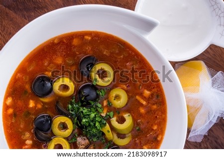 Soup with parsley, meat, olives, olives, carrots in a plate with sour cream and lemon on a wooden background