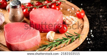 Raw tuna on a cutting board with garlic, tomatoes and spices. On a black background. High quality photo