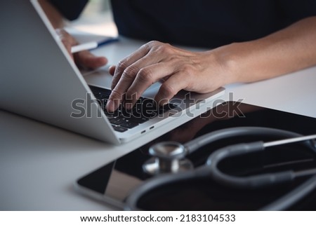 Close up of doctor, surgeon working on laptop computer with digital tablet on table in doctor's office, medical research, healthcare and medicine, electronic health record system concept