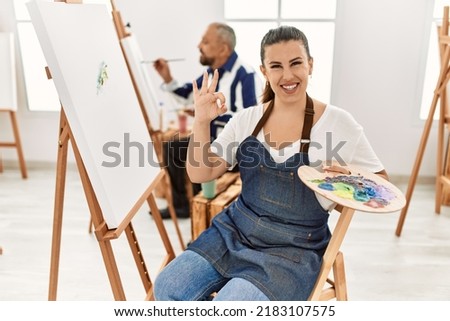 Young artist woman at art studio doing ok sign with fingers, smiling friendly gesturing excellent symbol 