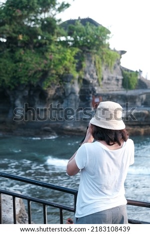 Young woman taking photos with her camera on Tanah Lot beach Bali during sunset.