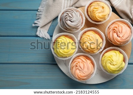Stand with tasty cupcakes on light blue wooden table, flat lay. Space for text Royalty-Free Stock Photo #2183124555
