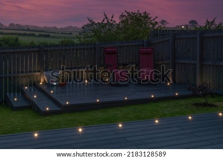 Ash grey composite decking built on two levels on a residential back garden with low voltage deck lights installed as well. Good Image for a landscape Gardiner Royalty-Free Stock Photo #2183128589