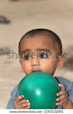 a cute baby boy playing with a ball on a muddy ground