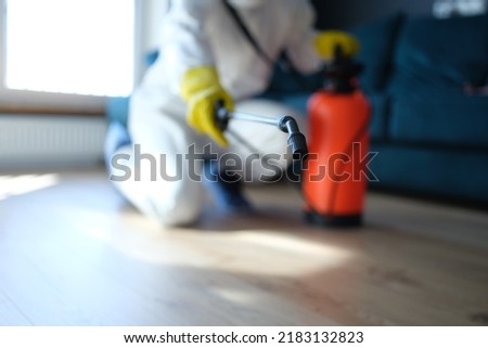 Person in white protective suit in hotel or apartment sprays disinfectant against viruses or rodents