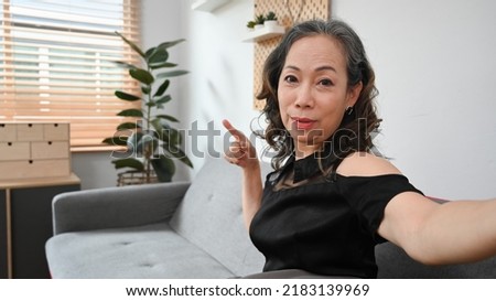 Joyful middle aged woman holding camera and taking selfie or recording stories for social network