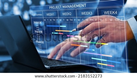 Project manager working on laptop and updating tasks and milestones progress planning with Gantt chart scheduling interface for company on virtual screen. Business Project Management System. Royalty-Free Stock Photo #2183152273