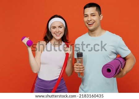 Young fitness trainer instructor sporty two man woman in headband t-shirt hold yoga mat hula hup bottle dumbbell spend weekend in home gym isolated on plain orange background. Workout sport concept