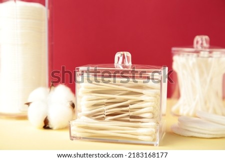 Cotton pads and cotton sticks in containers with cotton flower on red background. Top view