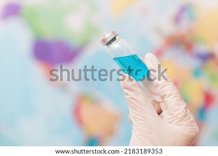 Doctor holds an ampoule with a vaccine on the background of the world map.  World vaccination concept.  The medicine is a liquid for injections of blue color.  medicine for treatment.