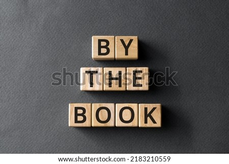 By the book - phrase from wooden blocks with letters, according to the rules  concept, gray background