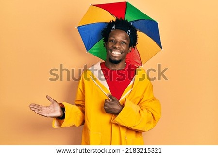Young african american man wearing yellow raincoat showing palm hand and doing ok gesture with thumbs up, smiling happy and cheerful 