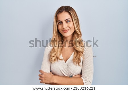 Young blonde woman standing over isolated background happy face smiling with crossed arms looking at the camera. positive person. 