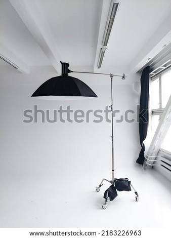 Professional photo flash light with a big softbox on a c-stand on a cyclorama in modern photo studio with a huge windows. Professional lighting equipment, flashes, c-stands.