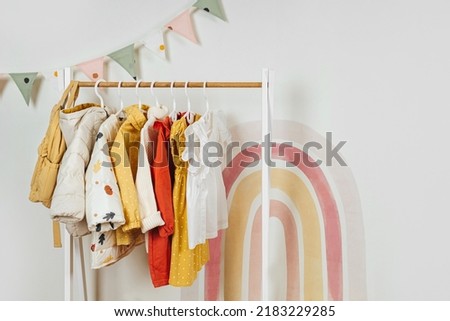 Wooden Clothing Rack with children's autumn outfits. Dresses, sweaters and jacket in kids room. Montessori wardrobe. Nursery Storage Ideas. 