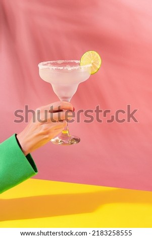 Female hand holding glass of delicious margarita cocktail isolated over pink yellow background. Cheers. Concept of cocktails, alcoholic drinks, taste, party, mix. Copy space for ad. Retro style Royalty-Free Stock Photo #2183258555