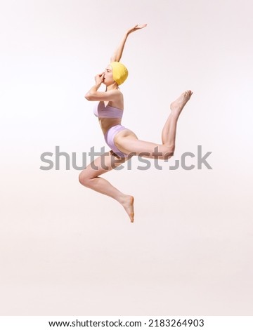Portrait of young woman in swimming suit and cap jumping into water isolated on grey studio background. Summer activity. Concept of beauty, fashion, vintage style, summertime, party. Copy space for ad