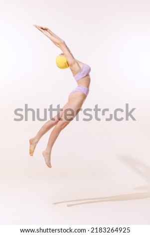 Portrait of young woman in swimming suit and cap jumping into water isolated over grey studio background. Fly jump. Concept of beauty, fashion, vintage style, summertime, party. Copy space for ad