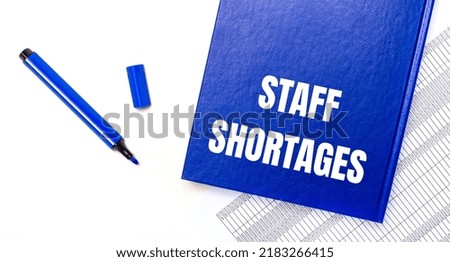 On a white background reports, a blue pen and a blue notebook with the text STAFF SHORTAGES. Business concept. Banner
