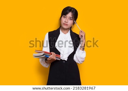 beautiful asian woman hug a book and thinking idea isolated on yellow background
