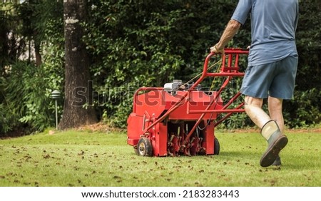 Man using gas powered aerating machine to aerate residential grass yard. Groundskeeper using lawn aeration equipment for turf maintenance. Royalty-Free Stock Photo #2183283443