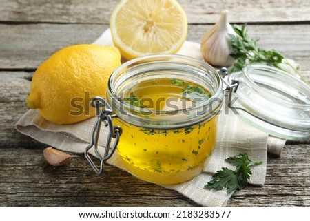 Jar with lemon sauce and ingredients on wooden table. Delicious salad dressing Royalty-Free Stock Photo #2183283577