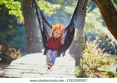 Beautiful autumn portrait of adorable preschooler girl in colorful maple leaves wreath on her head. Child having fun on garden swing or in hammock