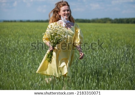 A young red-haired woman with a bouquet of field daisies runs along a green lawn