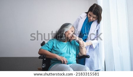 Asian woman doctor take care and encourage elderly patient Which sat on wheelchair, which she is saddened from depression, to elderly and  health care concept. Royalty-Free Stock Photo #2183315581