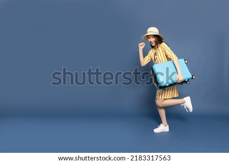 Happy young Asian woman traveler running and holding luggage isolated on blue background, Tourist female having cheerful holiday trip concept, Full body composition Royalty-Free Stock Photo #2183317563