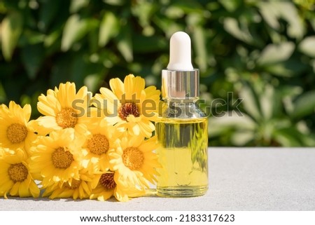 Transparent dropper bottle with calendula oil against green leaves as natural background. Making natural cosmetics at home. Herbal cosmetic oil for skincare or essential oil for aromatherapy. Mockup
