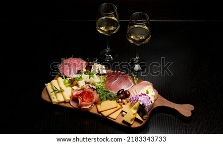 Two white wine glasses with buffet platter with cheese and meats, antipasti, prosciutto, charcuterie.
 Royalty-Free Stock Photo #2183343733
