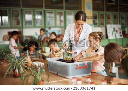 Science teacher assisting schoolgirl in planting seedlings during botany class at school. Royalty-Free Stock Photo #2183361741
