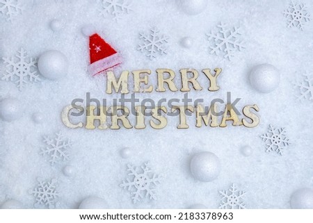 Merry christmas card, text in wooden letters on white snow, snowflakes, christmas hat. The concept of congratulation, invitation, holiday, promotions. High quality photo