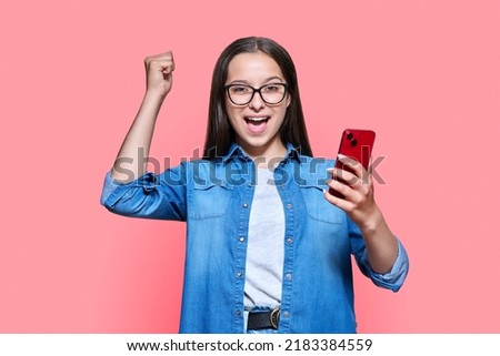 Happy teenage girl with smartphone, emotion yes success on red pink background