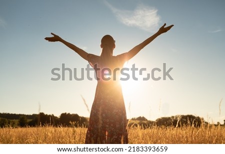 Young woman standing in meadow with with arms outstretched up to the beautiful sunrise sky. Freedom, feeling inspired and seeing the light concept.  Royalty-Free Stock Photo #2183393659