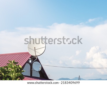 Round antenna on the roof of a house. Two white satellite television antennas on top of a private house against a blue cloudy sky Royalty-Free Stock Photo #2183409699