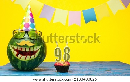 Funny watermelon in festive garlands for happy birthday greetings funny. Copy space watermelon with smile character. Happy birthday with number 98.