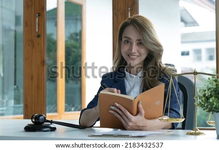 Confident and successful young Asian female lawyer or business legal consultant reading a law book or writing something on her notebook at her office desk.
