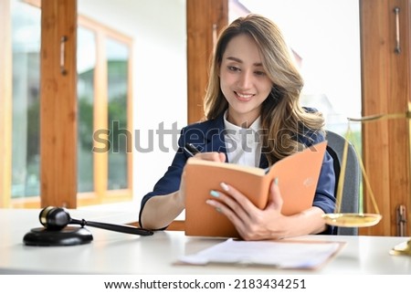 A beautiful young Asian female lawyer notes something on her personal book planner in the office. Lawyer, Attorney concept