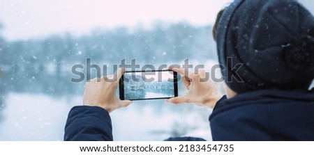the guy takes pictures on the phone of winter nature, hands take pictures of winter nature winter forest with river, hiking, winter holiday concept photo banner