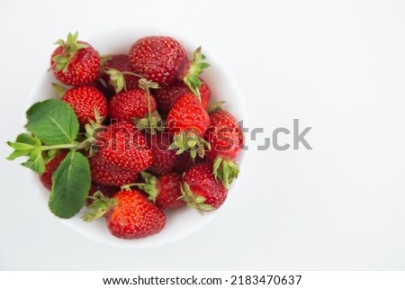 A white plate with strawberries and mint petals stands on the side on a white background in close-up with a place for text. High quality photo