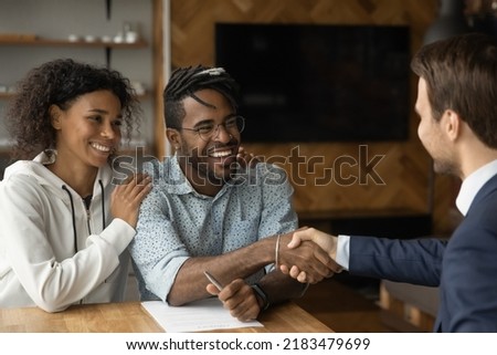 Happy African American couple shake hand close deal with male realtor or broker at meeting. Smiling biracial young family man and woman handshake make agreement with real estate agent in office.