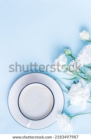 Morning cup of coffee and white eustoma flowers on blue pastel background. Creative breakfast for Woman day.