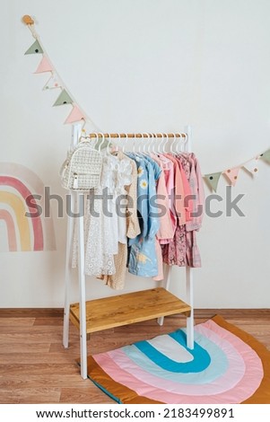 Wooden Clothing Rack with children's dresses, sweaters and jacket in kids room. Montessori wardrobe. Nursery Storage Ideas. Baby Girl Clothes.	 Royalty-Free Stock Photo #2183499891