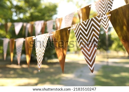 Golden bunting flags in park. Party decor Royalty-Free Stock Photo #2183510247
