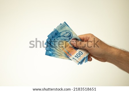 A spread of 100 Swiss Francs banknotes, held in hand by a Caucasian male. Close up studio shot, isolated on white background.