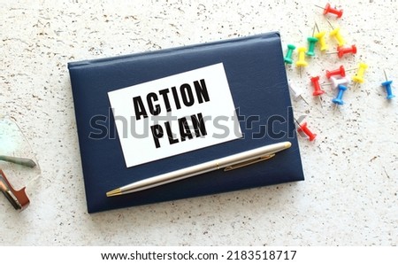 Text ACTION PLAN on a business card lying on a blue notebook next to the glasses.